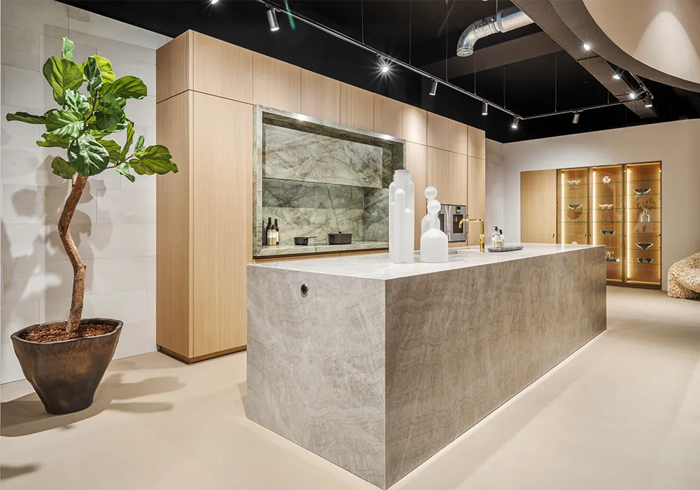 Cuisine design i-luminate avec façades en placage chêne clair et plan de travail en quartzite clair sur l'îlot central et la niche. Vitrines en laiton et buanderie dissimulée.